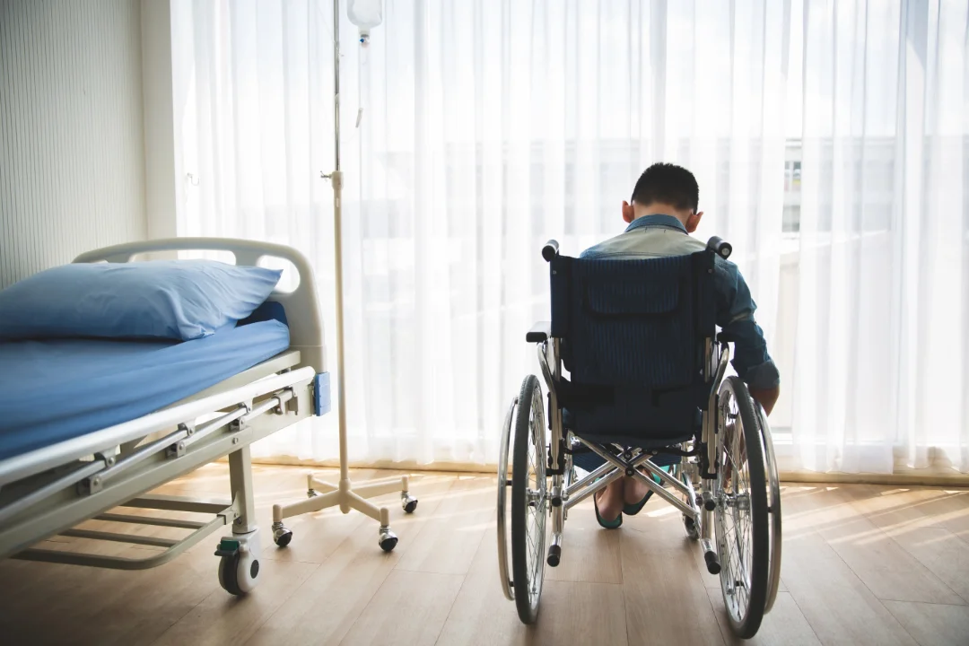 A person in a wheelchair beside a hospital bed
