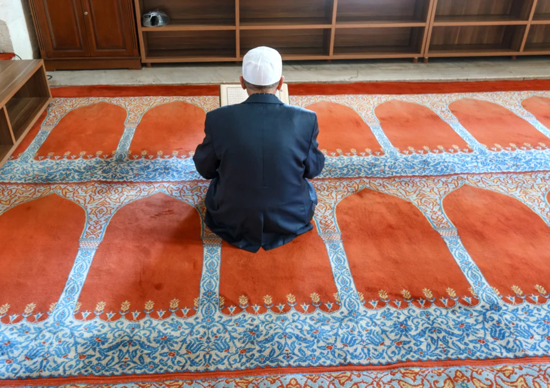 Older Muslim seated on a prayer rug in a mosque